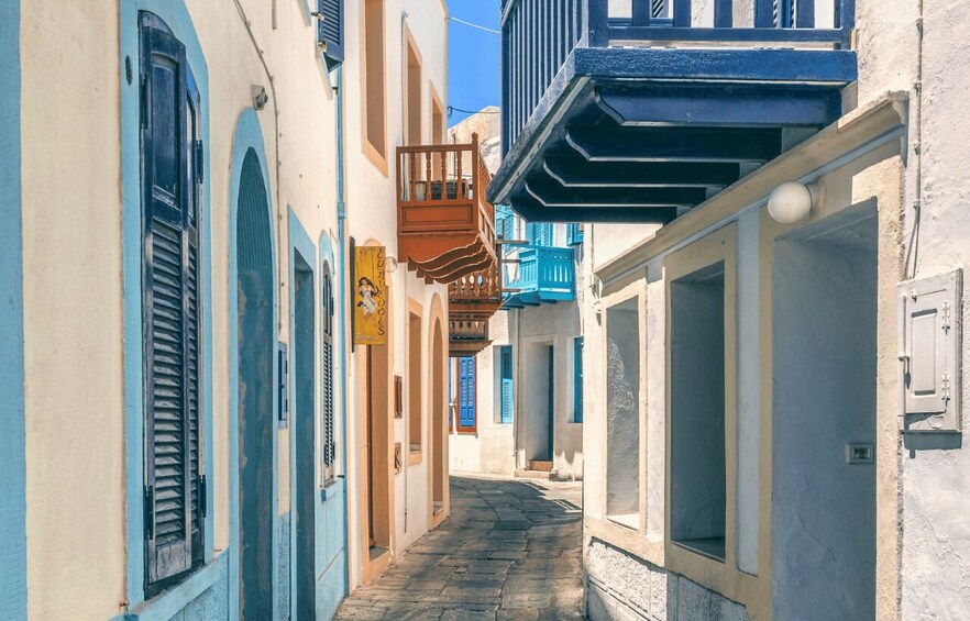 A narrow street with buildings painted in blue and white, featuring balconies and shutters. 4