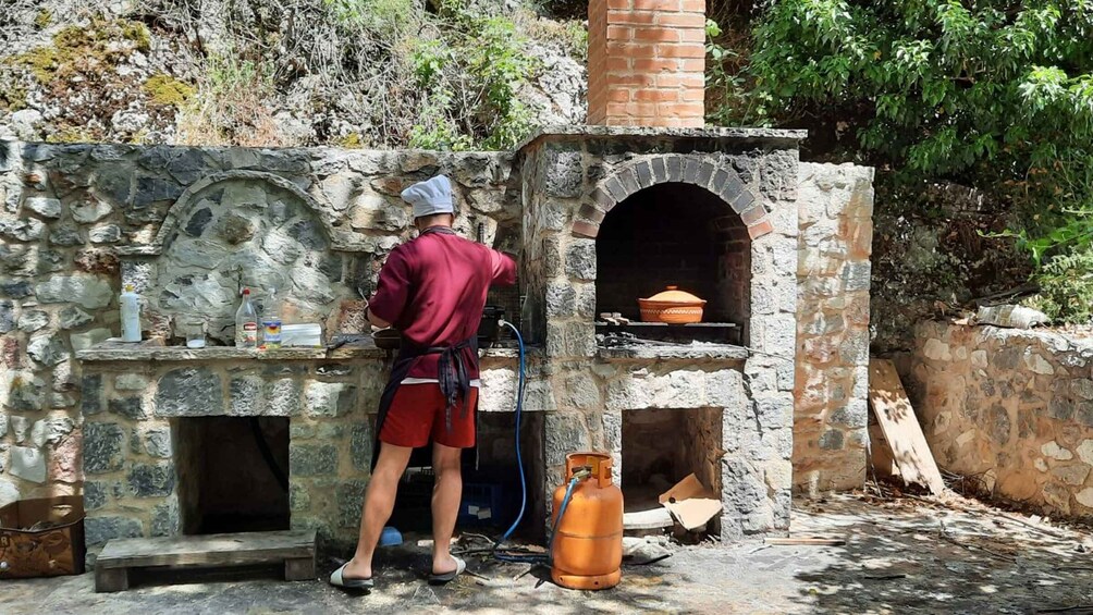 A chef cooking outdoors with a stone oven, surrounded by natural vegetation. 1
