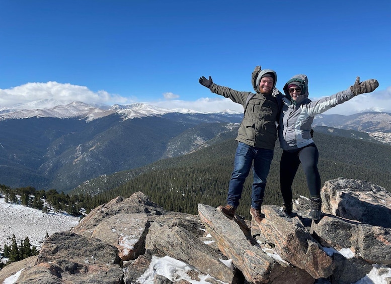 Two people standing on a rocky outcrop with a mountainous landscape in the background. 4