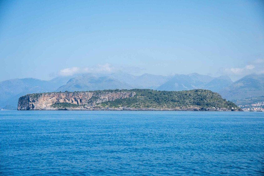 A coastal landscape with a prominent rocky cliff and a clear blue sea. 1