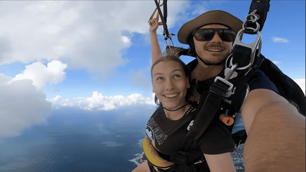 A person taking a selfie while skydiving with a clear view of the ocean and clouds below. 3