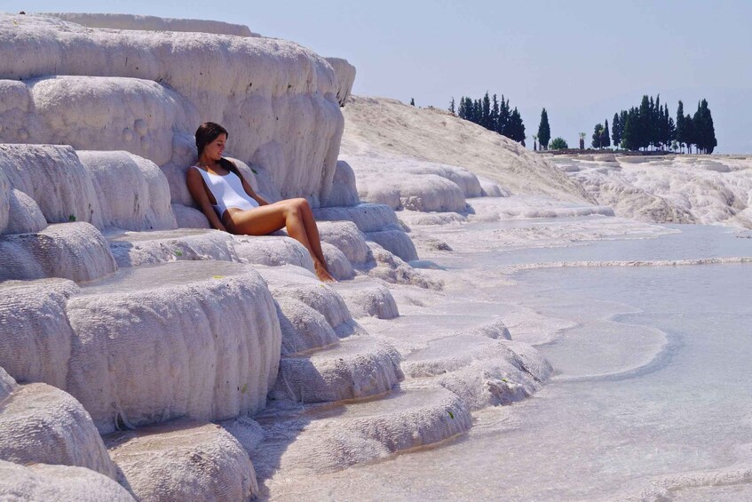 A person sitting on travertine formations in a natural setting with trees in the background. 5