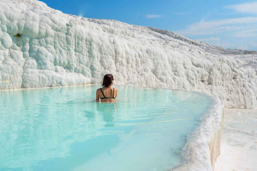 A person in a turquoise pool with white travertine formations in the background. 1
