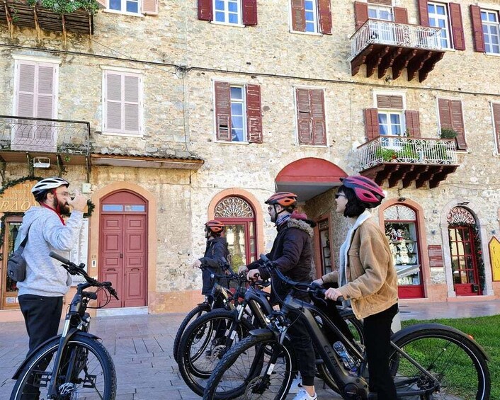 A group of people with bicycles in front of a stone building with red shutters and balconies. 4