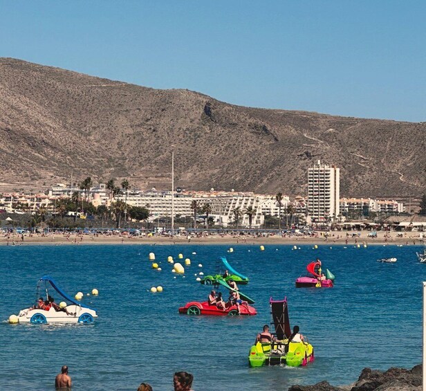 A beach with water taxis, a clear blue sea, and a mountainous backdrop. 5