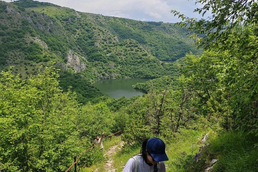 A person hiking on a trail with a lake and forested hills in the background. 3