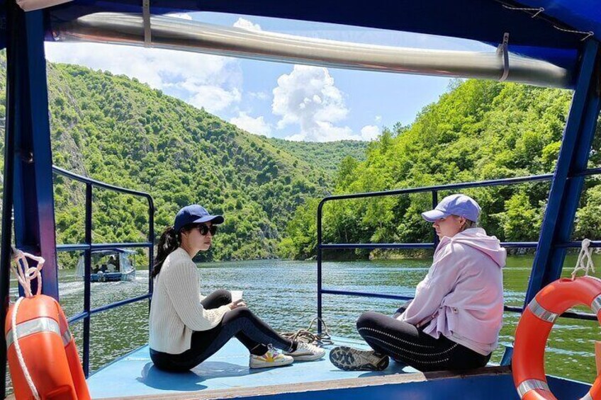 Two people sitting on a boat with a forested hillside in the background. 4