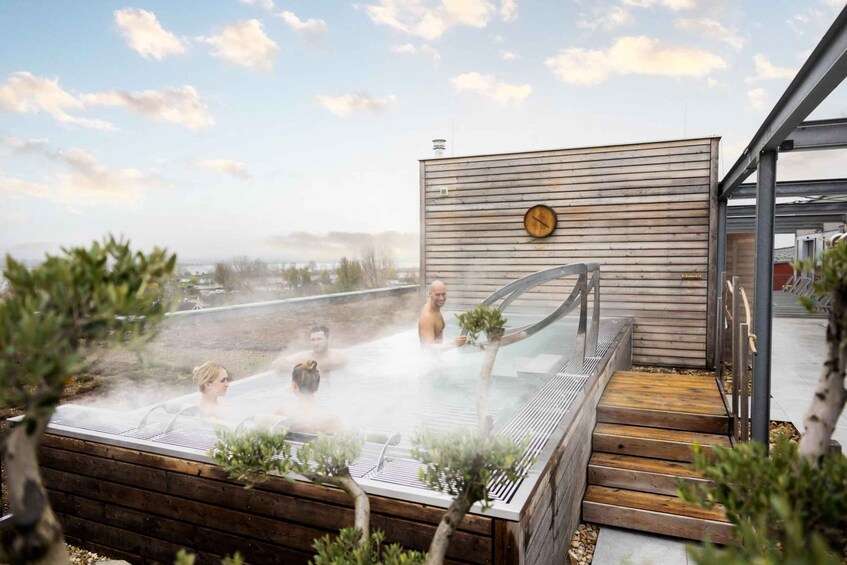 A hot spring with people relaxing, surrounded by wooden decking and greenery. 5