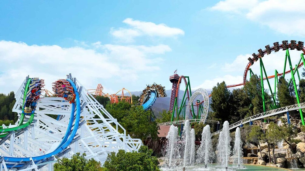 A theme park with roller coasters, water fountains, and a mountainous backdrop. 2