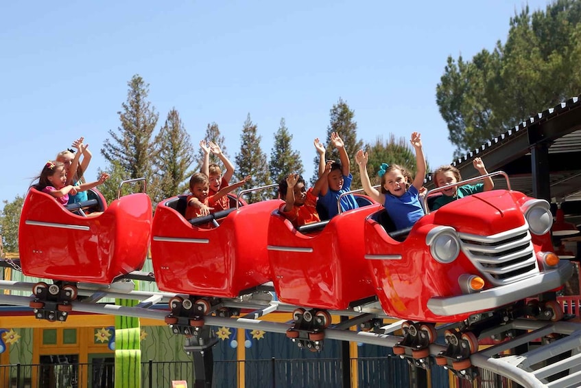 A group of people on a red roller coaster with a clear sky and trees in the background. 4