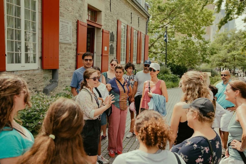 A group of people gathered outdoors in front of a building with red shutters and stone walls. 2