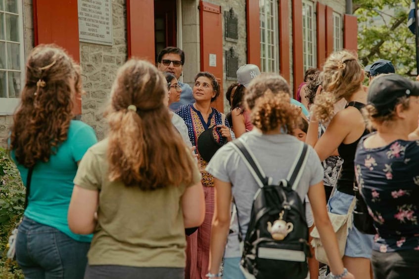 A group of people standing in front of a building with red shutters and stone walls. 4