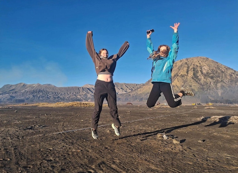 Two people jumping in a volcanic landscape with mountains in the background. 3