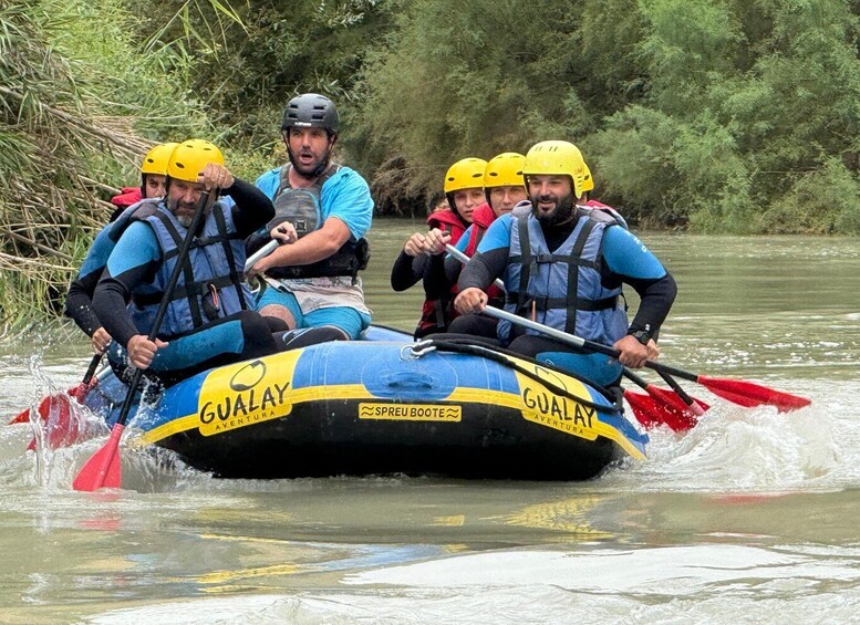 A group of people in a blue and yellow raft with 'GUALAY AVENTURA' written on it, paddling through a river surrounded by greenery. 5