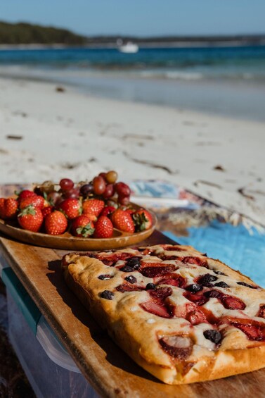 A beach scene with a wooden table holding a pizza and a bowl of strawberries. 3