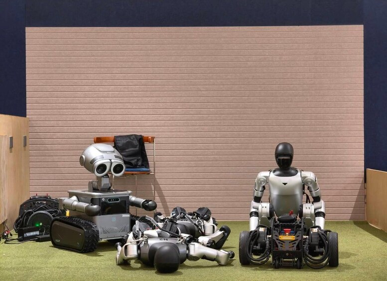 Two robots, one with a camera and the other with wheels, in front of a wall with a bench and a jacket. 4