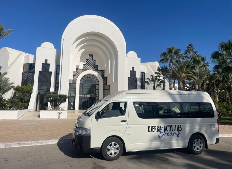 A white van parked in front of a modern building with arched windows and palm trees. 1
