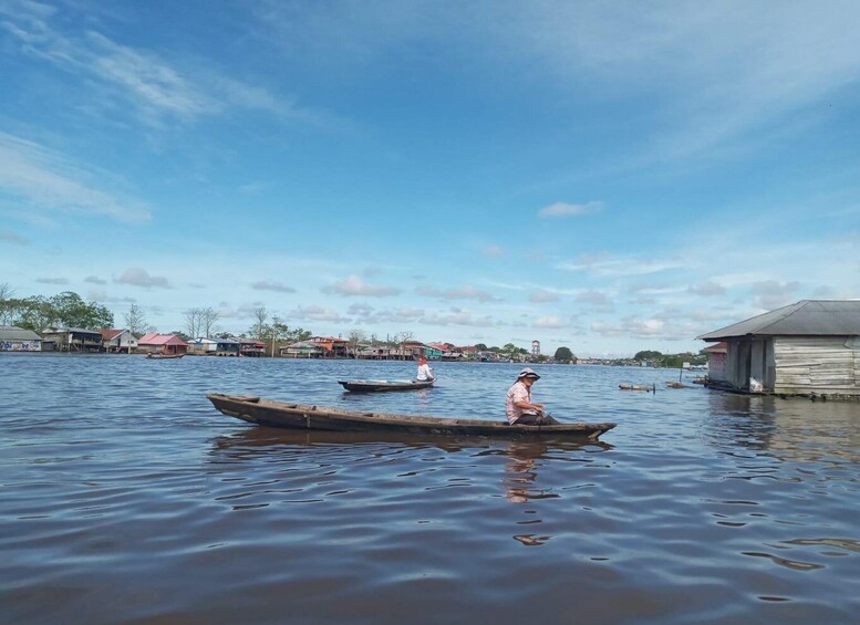 A calm river with wooden boats, a person rowing, and houses along the riverbank. 1