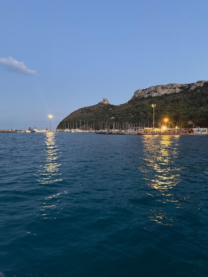 A calm sea with reflections of lights, a rocky hill, and a small building. 4