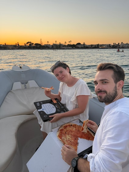Two people on a boat with pizza boxes and slices. 2