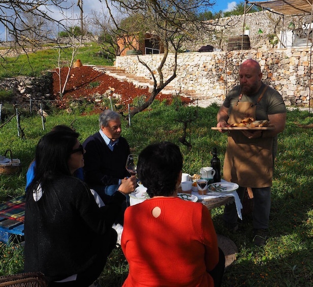 A group of people dining outdoors with a stone wall and greenery in the background. 3
