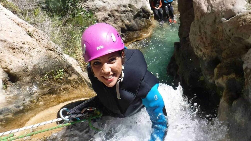 A person in a wetsuit and helmet near a water body with rocks. 3