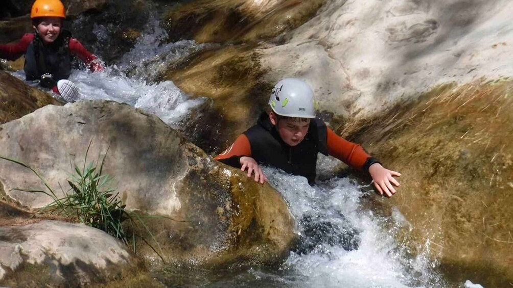 Two individuals navigating a white water stream with rocks. 1
