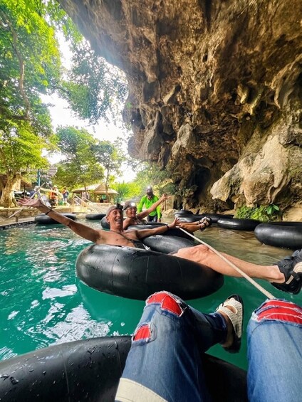 People floating on water in a natural setting with a rocky cliff and trees. 1