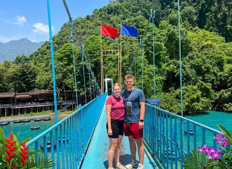 A suspension bridge with two people standing on it, surrounded by lush greenery and a mountainous landscape. 2