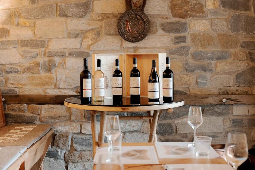 A stone wall with a wooden table displaying wine bottles and glasses. 1