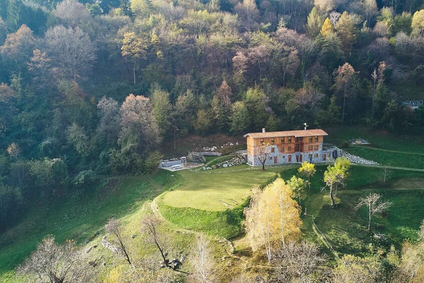 A large wooden house surrounded by a stone wall, set in a lush green landscape with trees and a small pond. 4