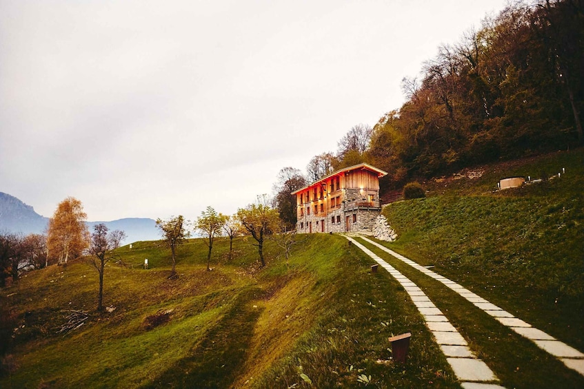 A stone house with a wooden facade on a hillside, surrounded by trees and a clear sky. 2