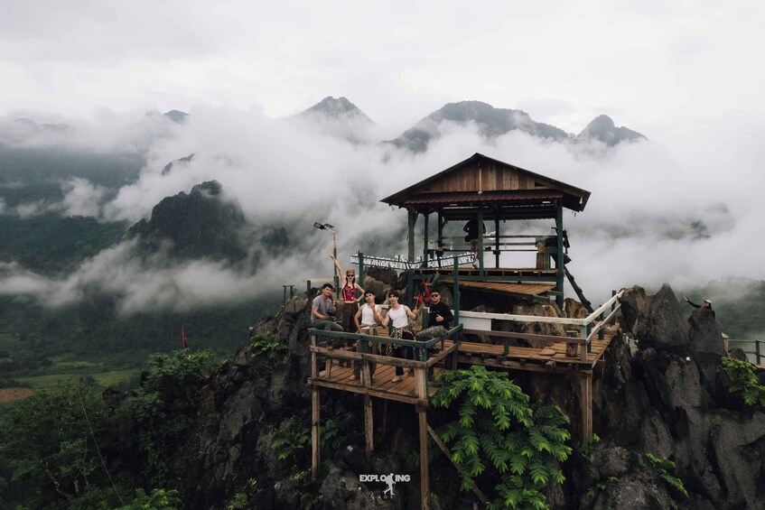 A wooden observation tower with people standing on it, overlooking a mountainous landscape with clouds. 1