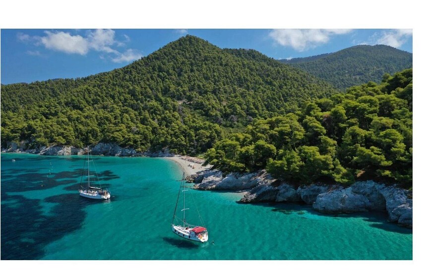 A turquoise sea with boats, a sandy beach, and a forested mountain. 1