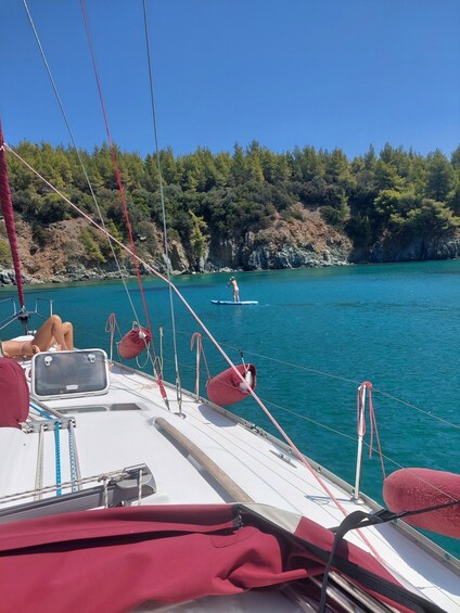 A sailboat with a person paddleboarding in the background, surrounded by clear turquoise water and a forested coastline. 4