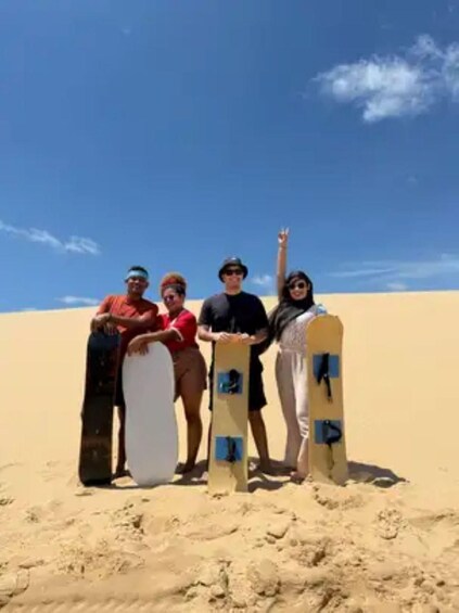 Four people standing on a sandy beach with surfboards, under a clear blue sky. 4