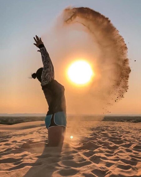 A person standing on a sandy beach with the sun low on the horizon, casting a warm glow. 2