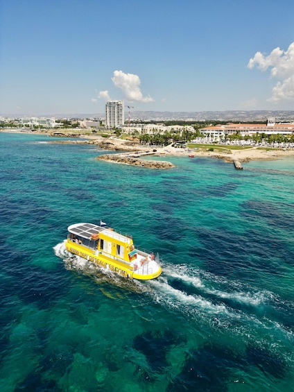 A yellow boat with a website URL on its side, cruising through clear blue waters with a coastal cityscape in the background. 2