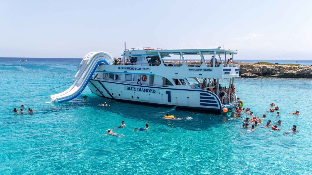 A boat with a water slide and people swimming in the water. 5