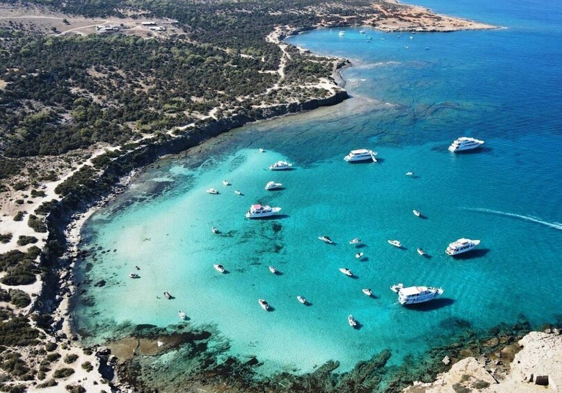 An aerial view of a coastal area with clear turquoise waters, numerous boats, and a mix of forested land and sandy beaches. 1