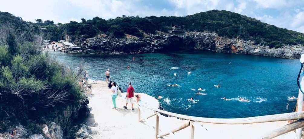 A coastal area with people swimming in the water, a sandy beach, and a rocky landscape with greenery. 2