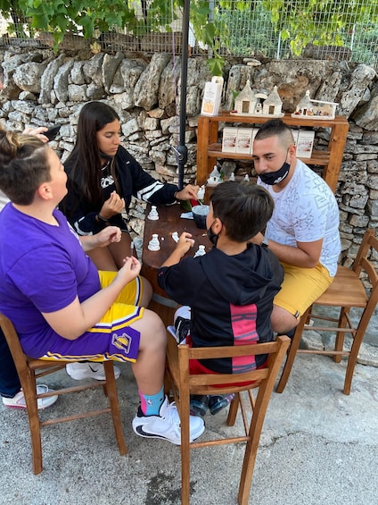 A group of people playing a board game outdoors at a table with a stone wall in the background. 4