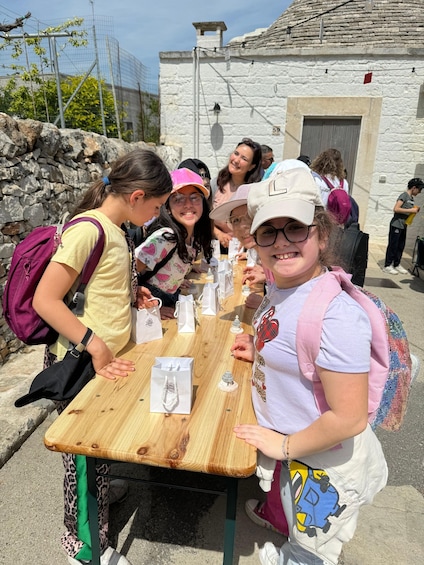 A group of people sitting at a wooden table outdoors with a stone building in the background. 5
