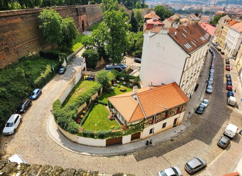 A cobblestone street with parked cars, a roundabout, and a building with a tiled roof. 5