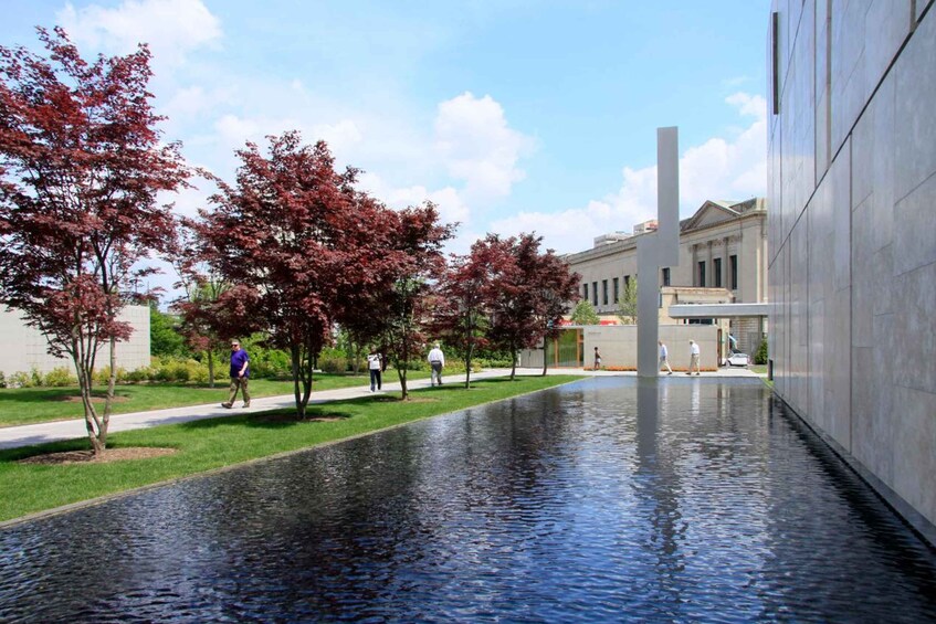 A water feature with people walking along a path lined with trees and a modern building in the background. 3