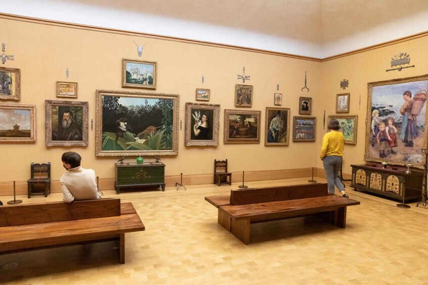 An art gallery with various paintings on the walls and benches for visitors to sit on. 2