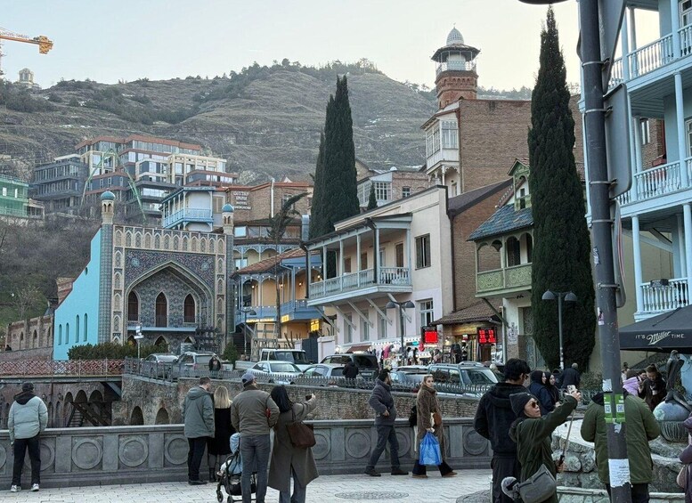 A bustling street with historic buildings, a prominent mosque, and a hillside in the background. 4