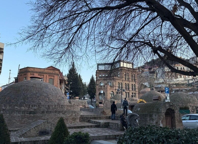 A historical site with stone structures, a building with arched windows, and a tree with bare branches. 5