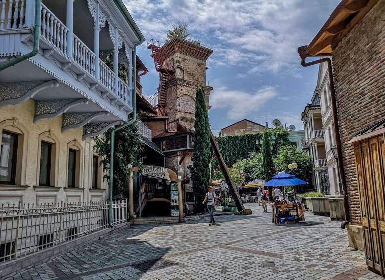 A cobblestone street with historic buildings, a tower, and a market stall. 1