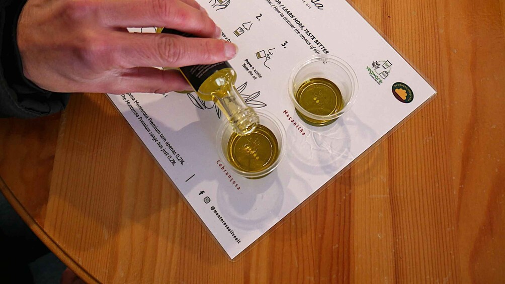 A person pouring oil from a bottle onto a paper with text and two small containers. 3